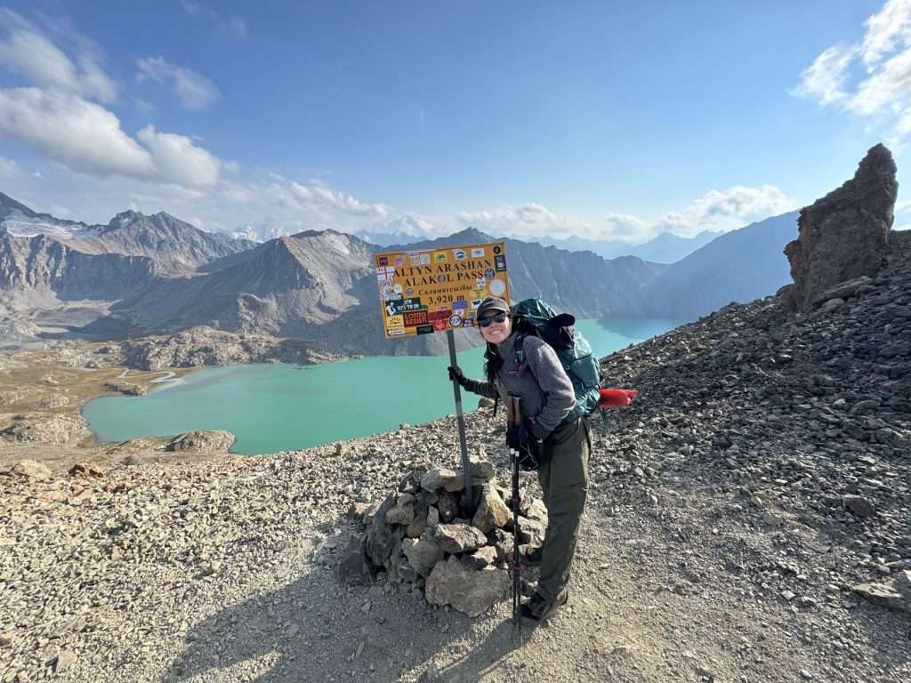 The narrator with an Ala Kol pass sign and the lake.
