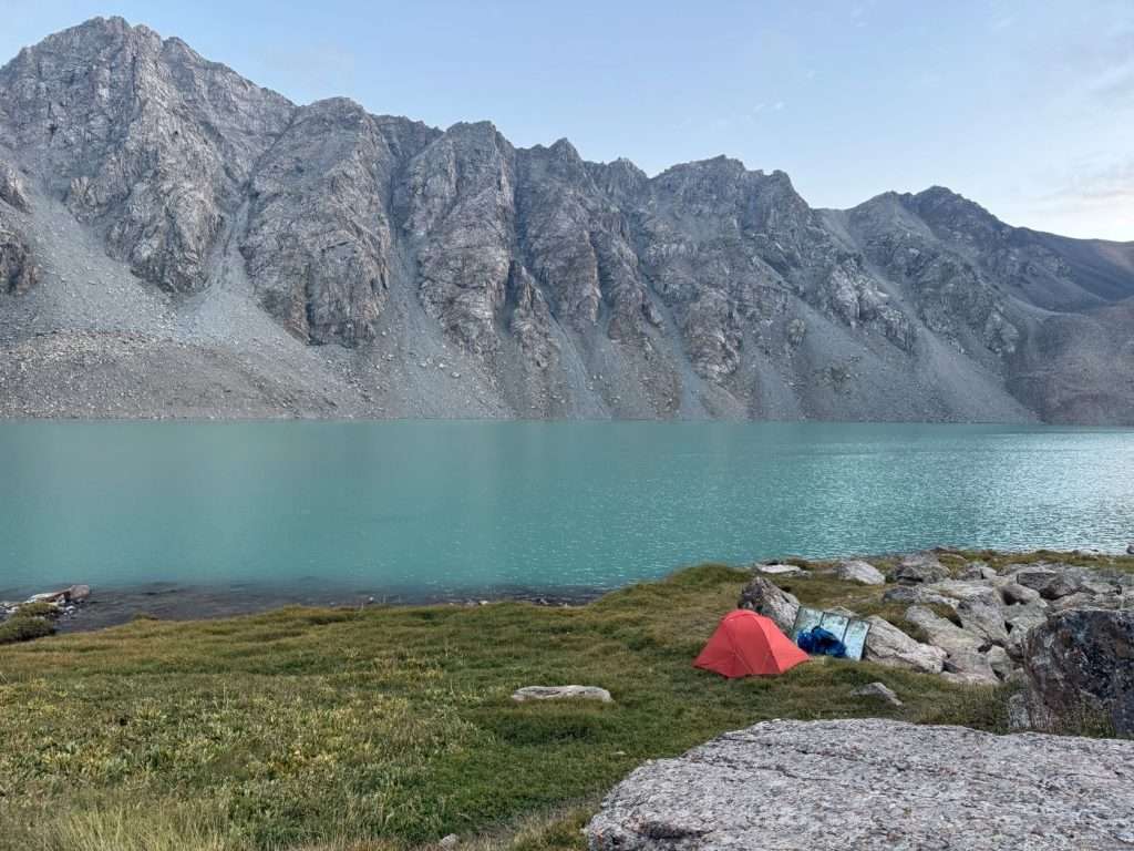 An orange tent set up beside the turquoise blue Ala Kol lake.
