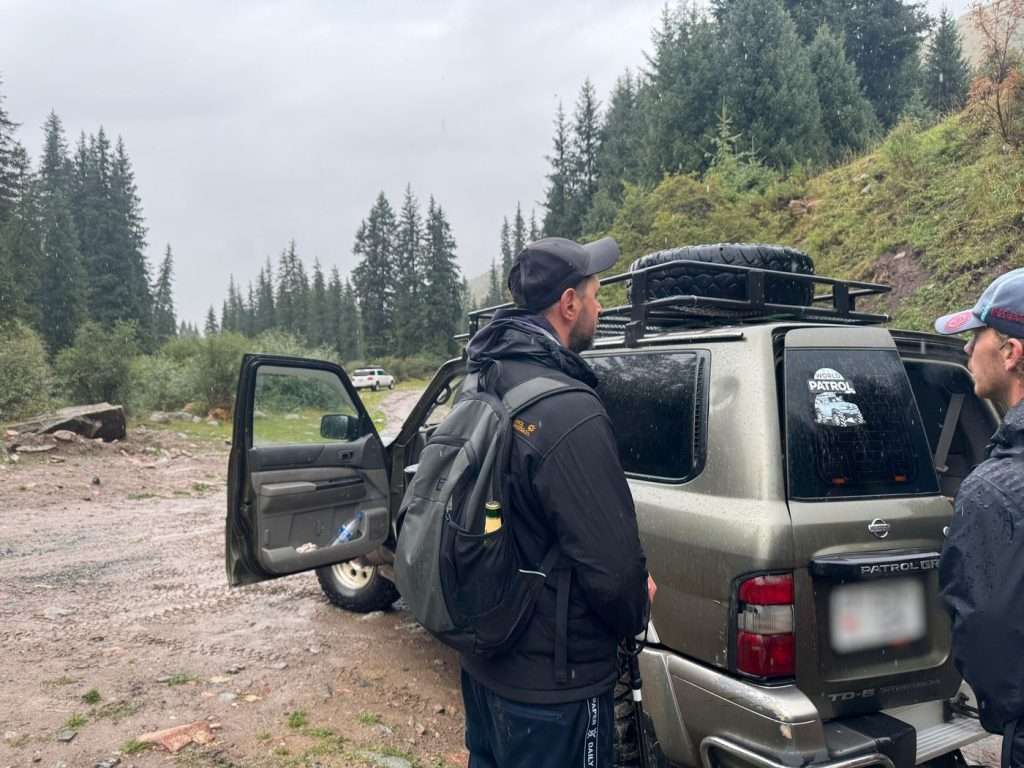 Two hikers discuss shared taxi prices from Karakol River to Karakol.
