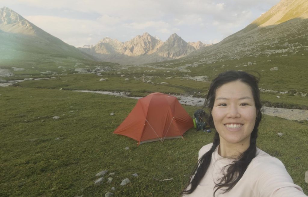 Solo female hiker with an orange tent in a valley with mountains in the background
