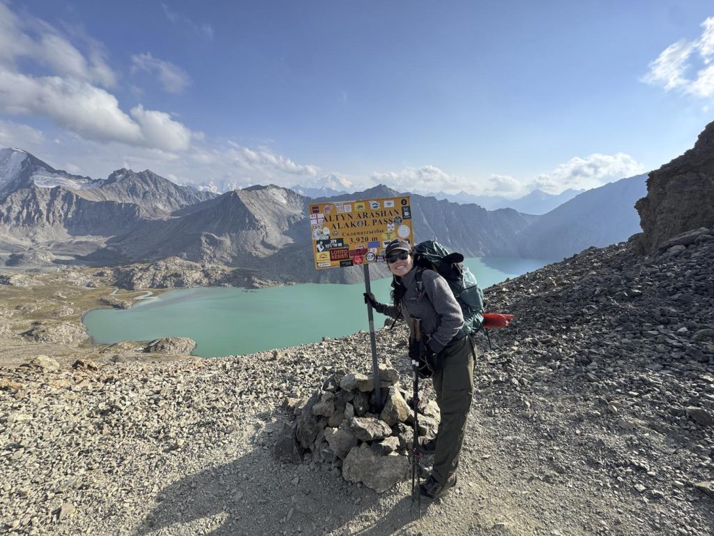 Solo hiker posing with Altyn Arashan Alakol Pass sign at 3920 meters